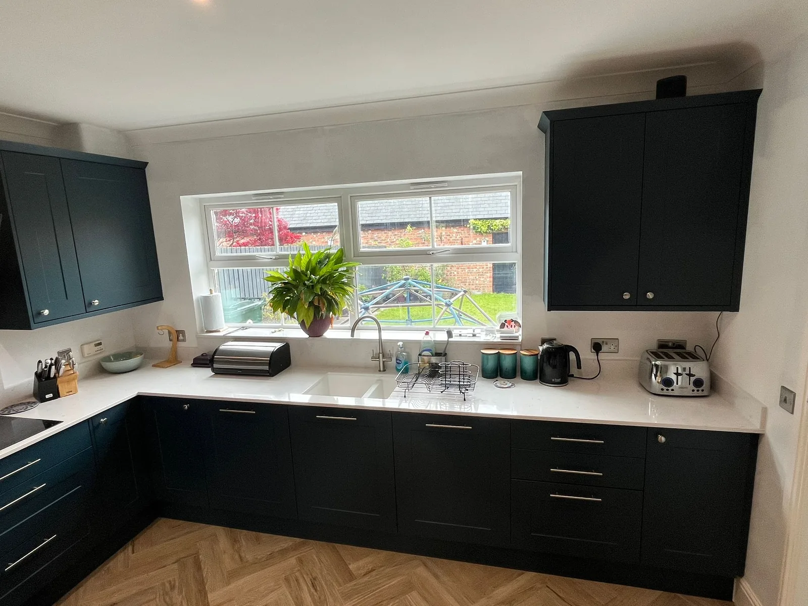 Finished navy kitchen run with quartz worktop, sink under the window and herringbone floor