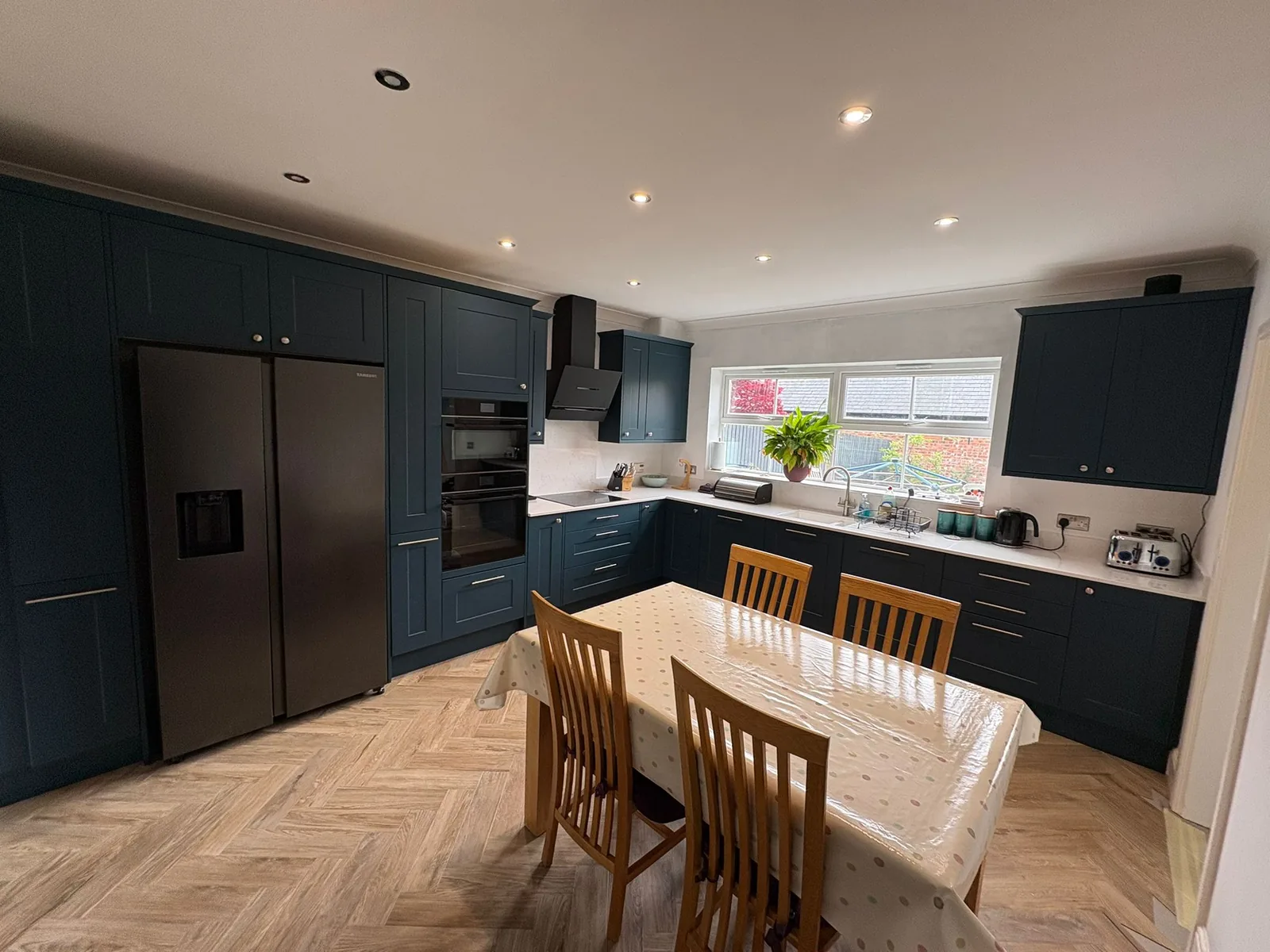 Open plan navy kitchen and dining area with herringbone flooring, finished and in use